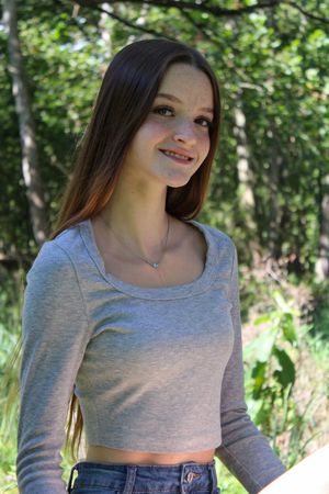 A person wearing a gray crop top poses outdoors against a green leafy background in natural lighting.