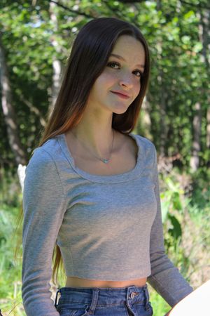 Someone in casual attire lounges against a tree trunk in a sunlit forest setting.
