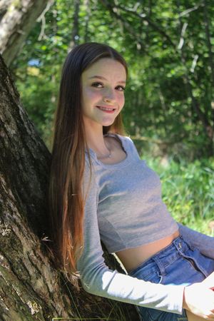 A casual outdoor photoshoot featuring someone in a gray top and denim against a wooded backdrop.