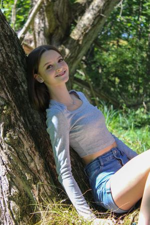 A casual portrait in nature showing someone lounging by a tree in summer attire.