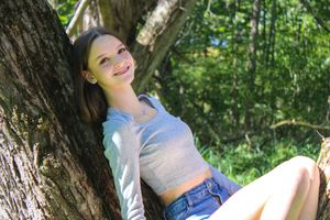 Someone relaxes outdoors wearing a gray top and jeans in a wooded setting.