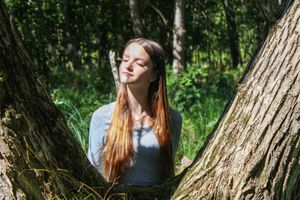 A peaceful outdoor portrait against a tree trunk in a sunlit forest setting.