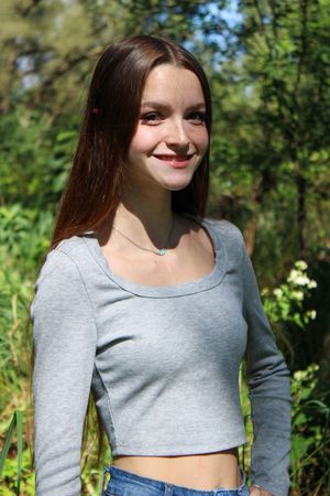 Casual outdoor portrait in grey crop top with sunny forest backdrop.