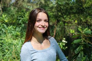 Candid outdoor portrait with bright natural lighting and green foliage.