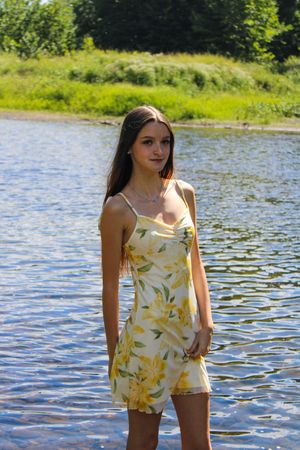 A person stands in a yellow floral romper against sparkling water and green summer landscape.