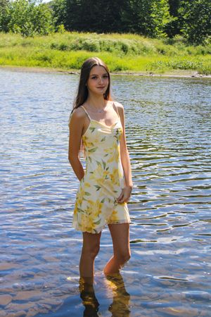 Someone wades in shallow river water wearing a light-colored floral outfit on a sunny afternoon.