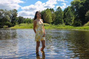 Scenic river view with someone standing in shallow water against a backdrop of trees and blue sky.