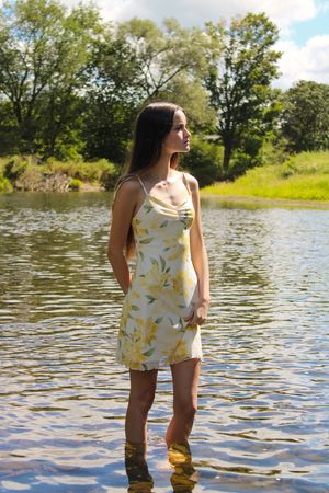 Someone wearing a yellow floral romper stands in shallow lake water on a sunny summer day.