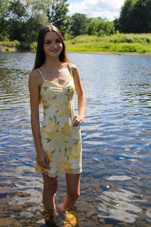 A person in a light summer outfit wades through shallow water near a grassy shoreline.