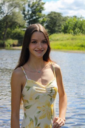 Someone poses in a white and yellow floral dress by a serene lake on a bright summer day.