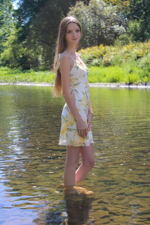 Someone wades in shallow lake water wearing a light-colored summer outfit.