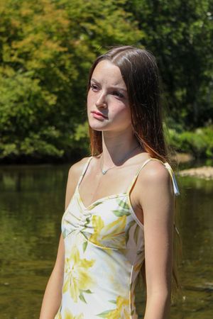 A woman in a floral sundress poses against a serene lake backdrop on a sunny summer day.