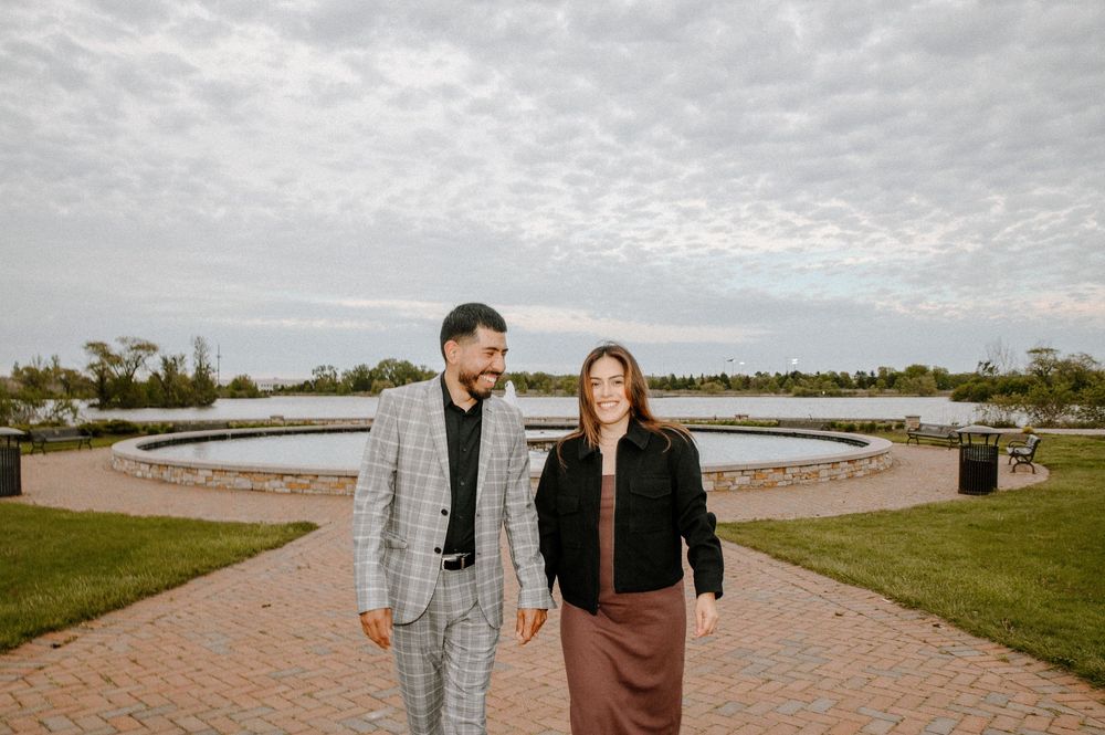 Two people walk together on a brick pathway near a circular fountain on an overcast day.