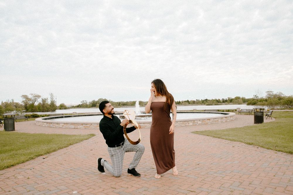 A romantic proposal takes place on a brick pathway with a circular garden backdrop.