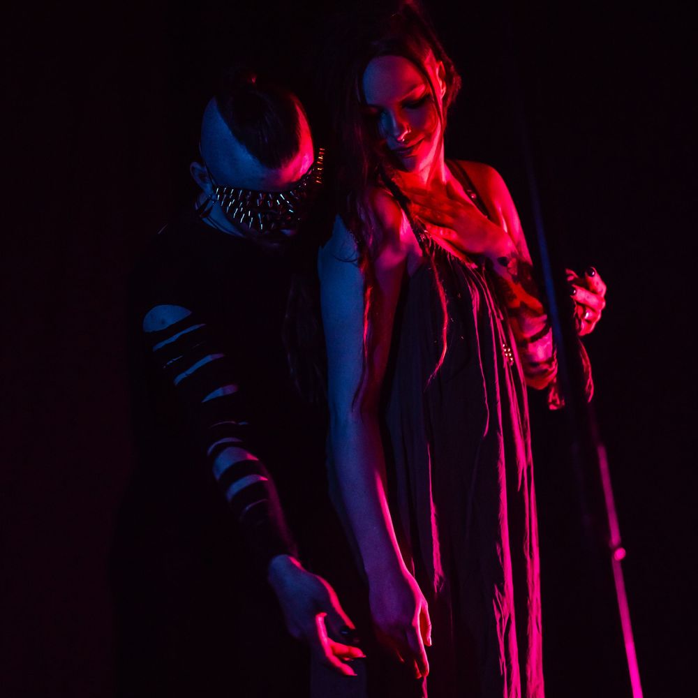 Figure lit with dramatic red and blue lighting stands in theatrical pose against dark background.