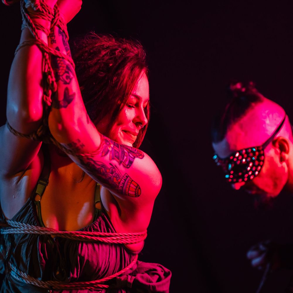 Dramatic red stage lighting illuminates silhouettes of performers during an intimate dance sequence.