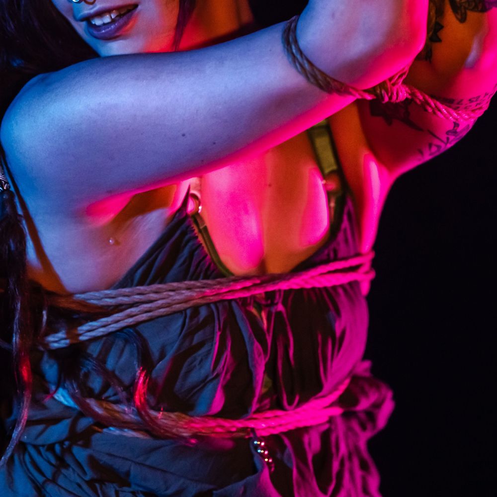 Artistic nude female silhouette poses against colorful pink and blue lighting in moody boudoir photoshoot.
