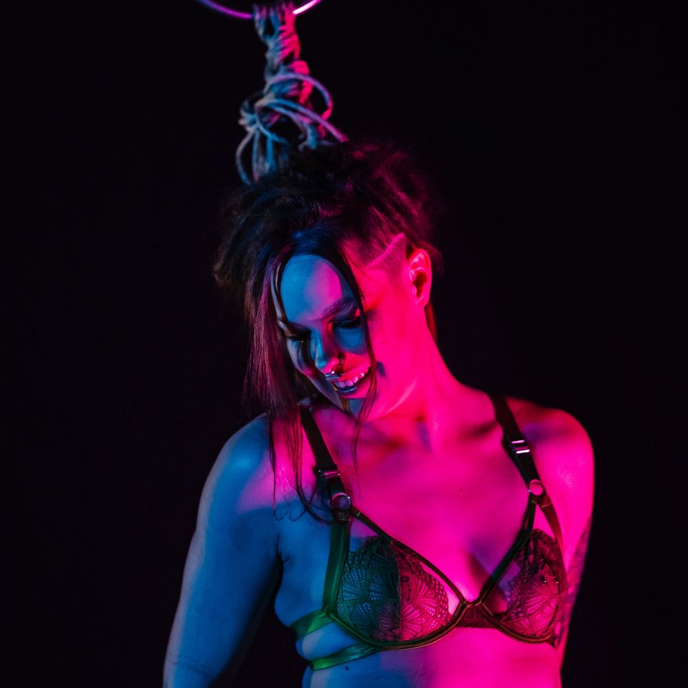 Artistic portrait in vibrant neon lighting with pink and blue colors creating a dramatic shadowy atmosphere.