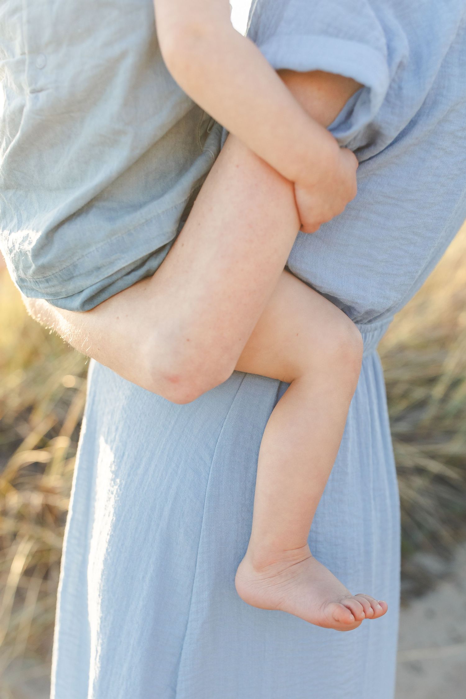 A series of close-up photos showing small bare feet being held against a light blue dress in a natural outdoor setting.Film by Chelsee Rawe