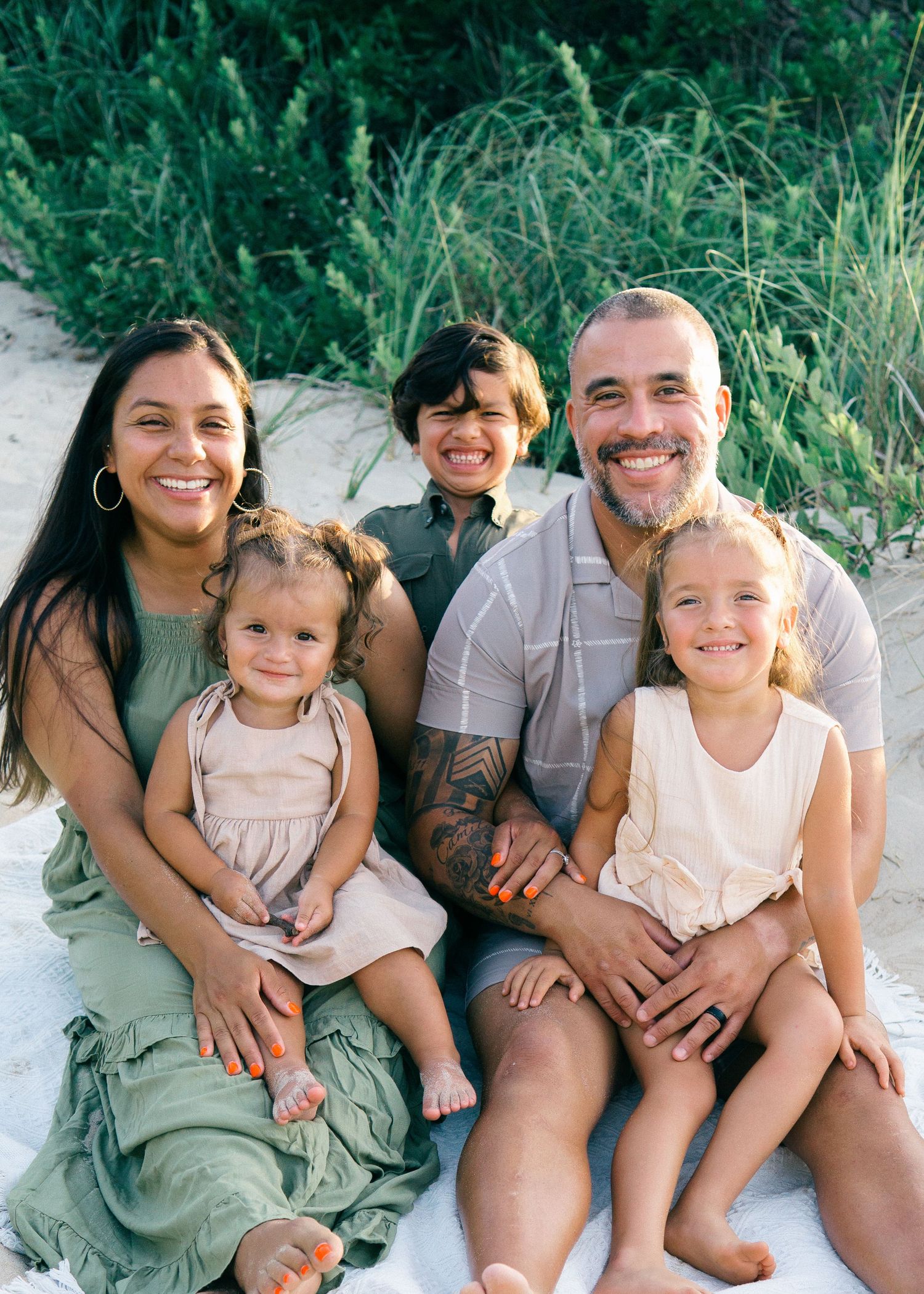 Smiling family of 5 sitting on a Cape Cod beach at sunset, lighthearted and candid.