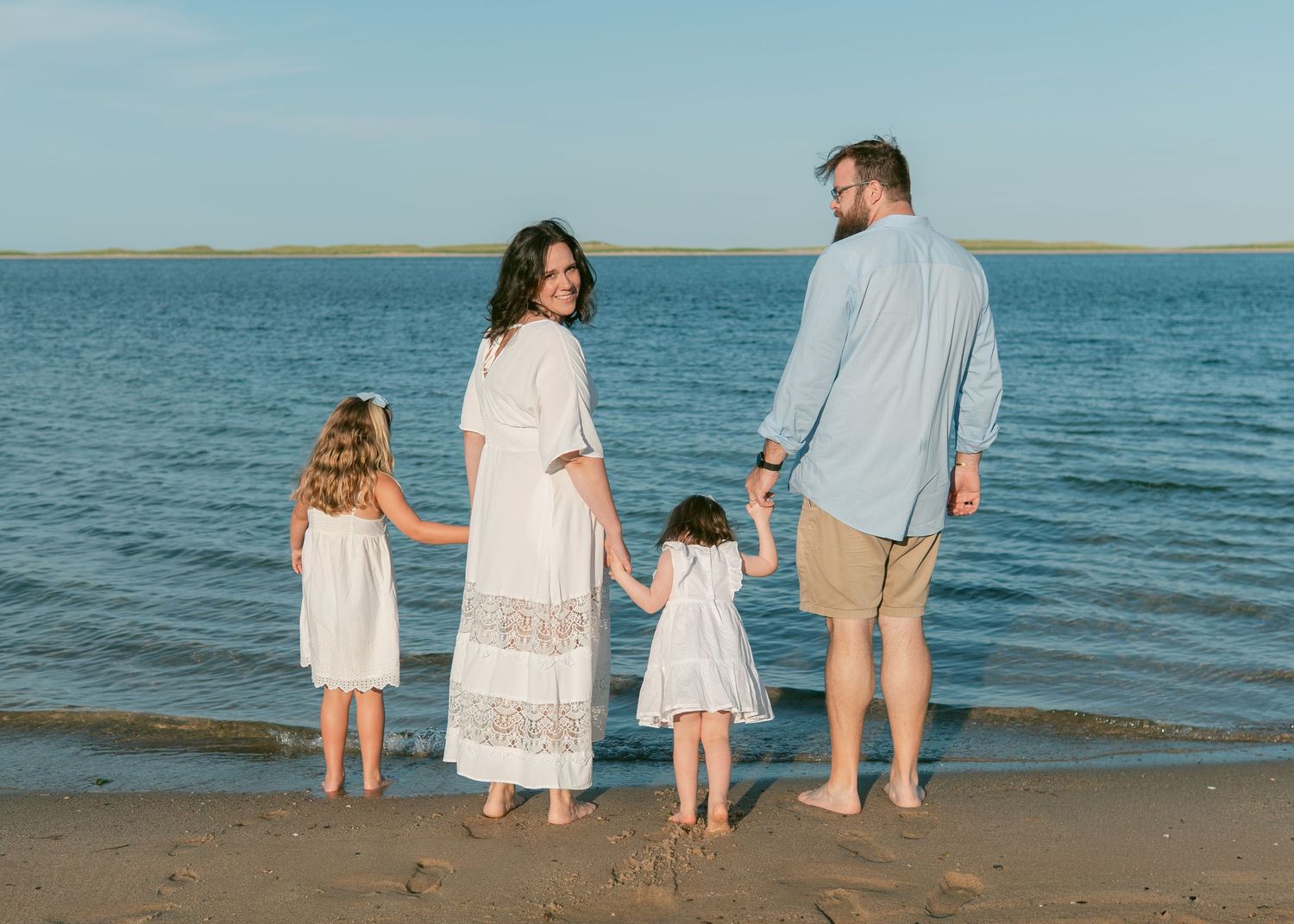 Smiling family of 5 sitting on a Cape Cod beach at sunset, lighthearted and candid.