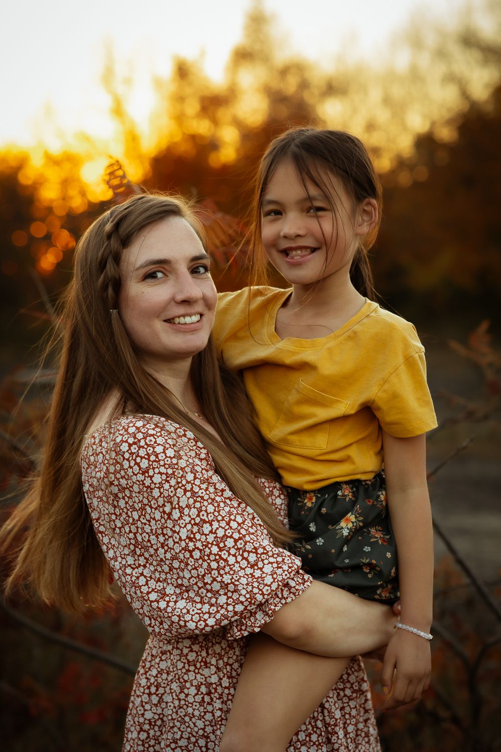 Two people in warm sunset lighting embrace outdoors with one wearing a floral dress and the other in yellow.