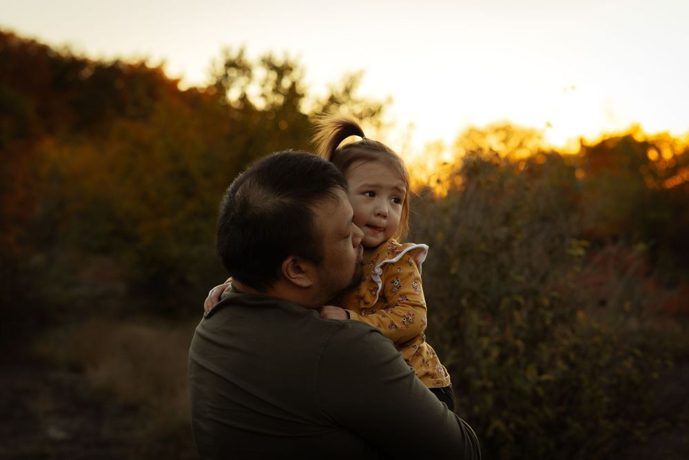 A couple embraces in silhouette against a warm golden sunset with trees and foliage in the background.