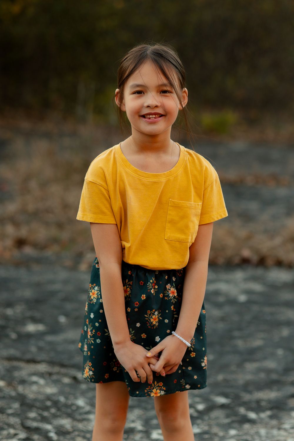 Child in bright yellow t-shirt and floral shorts poses outdoors against rocky natural backdrop.