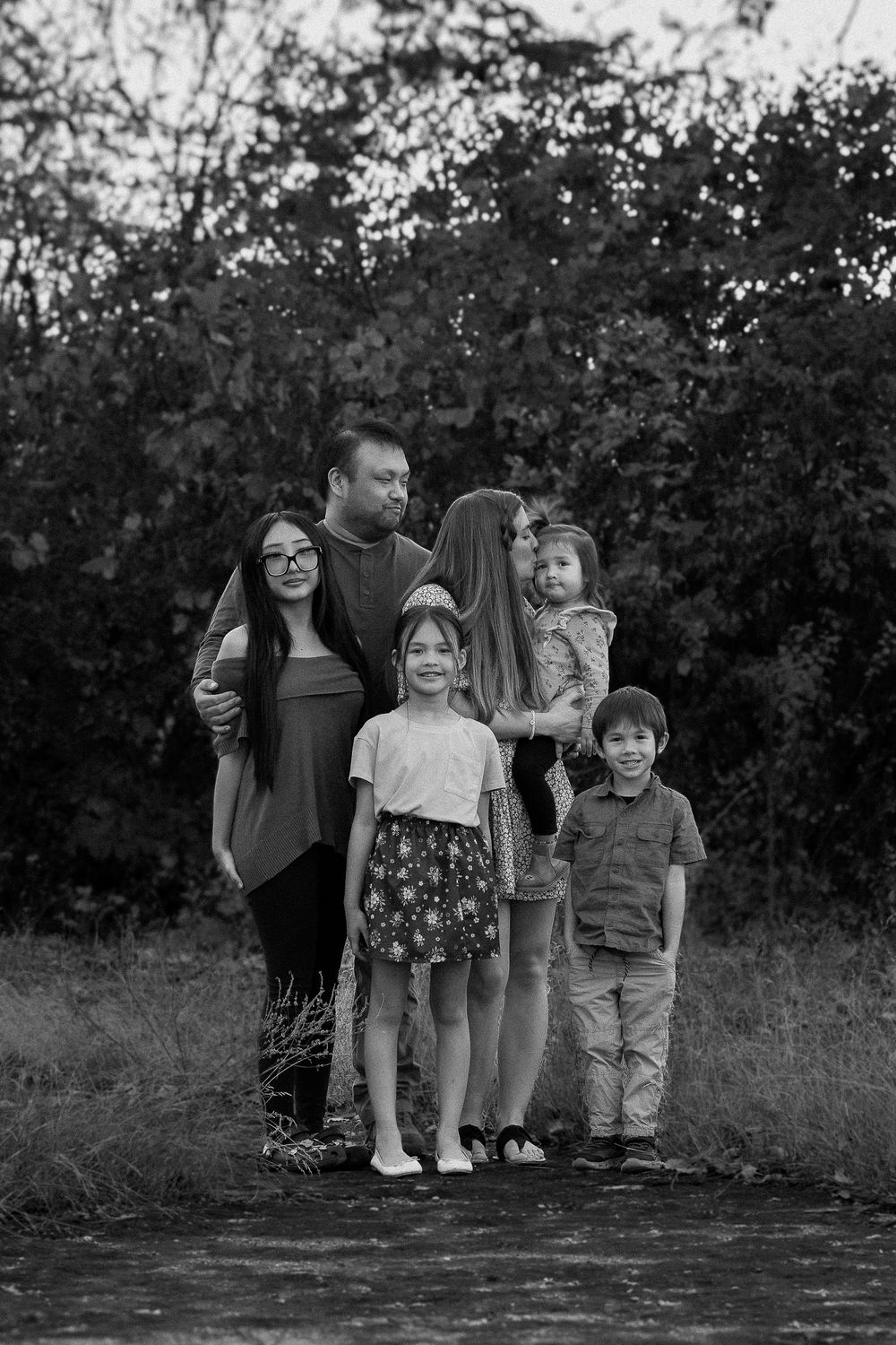 A black and white photo series of a family posing together outdoors with trees in the background.