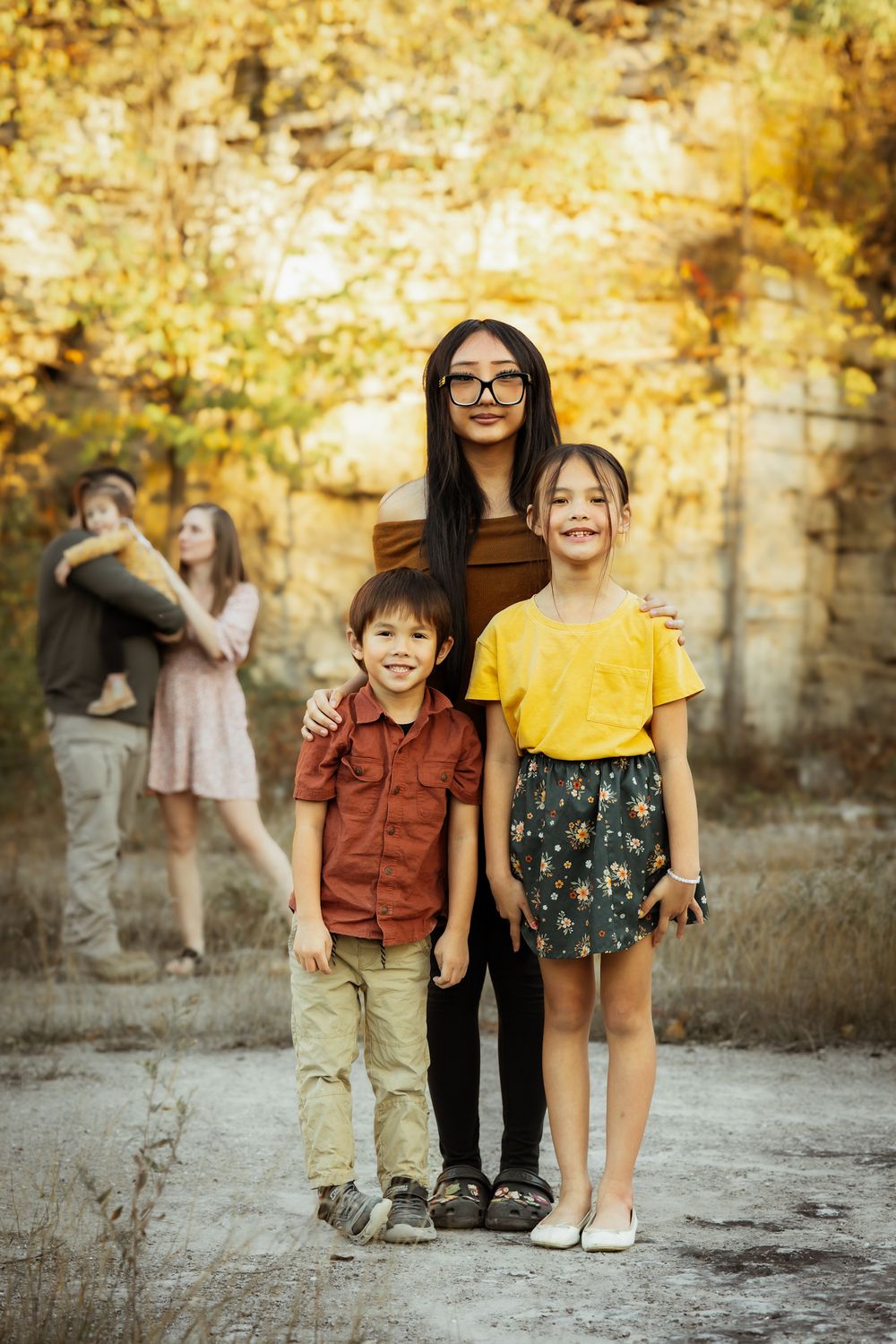 Two young children standing together outdoors against a vibrant autumn background with golden sunlight.