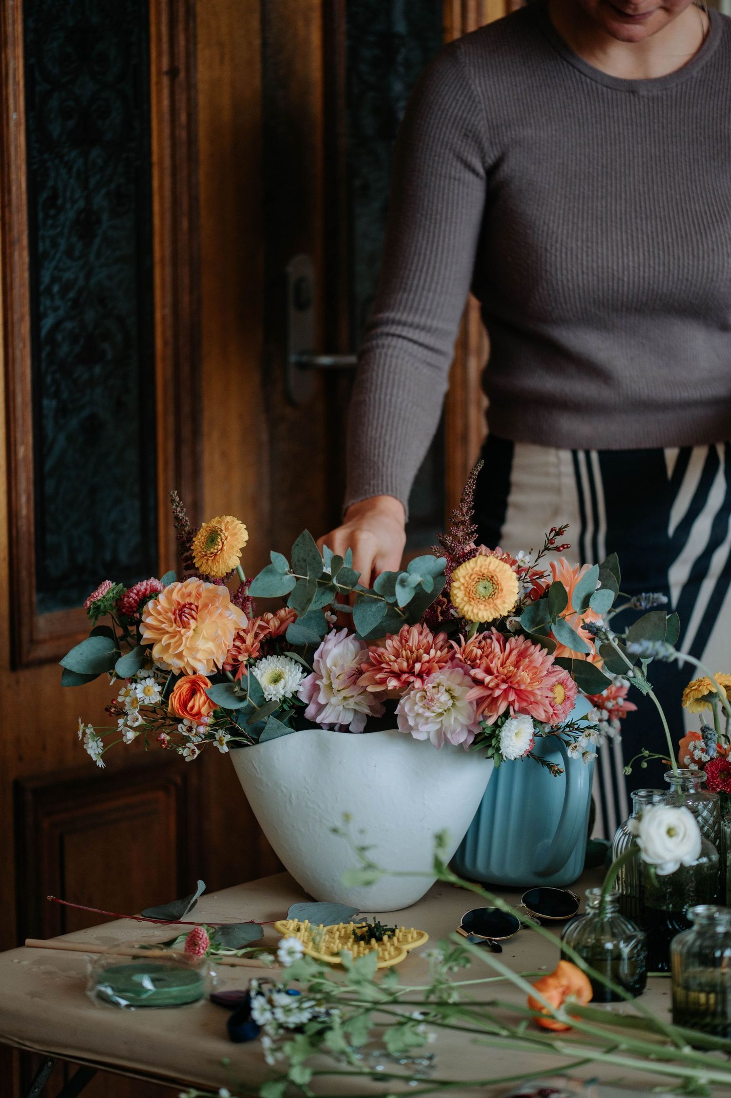 A rustic table setting features delicate floral arrangements in white bowls with peach and coral blooms.