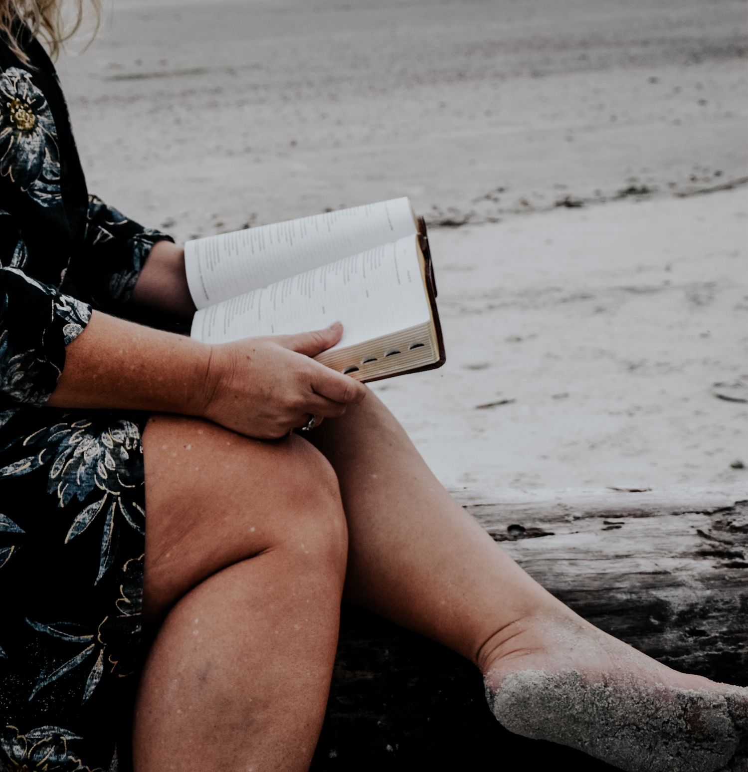Person in floral print jacket with windswept hair dancing on a cloudy beach at dusk.