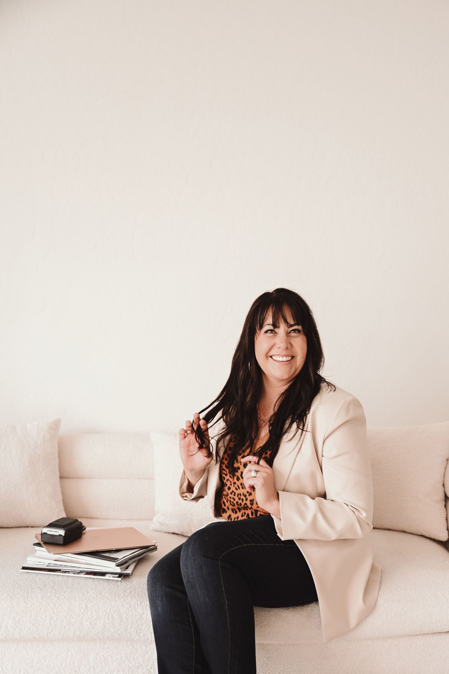 Professional photoshoot on white couch wearing leopard print and cream blazer.