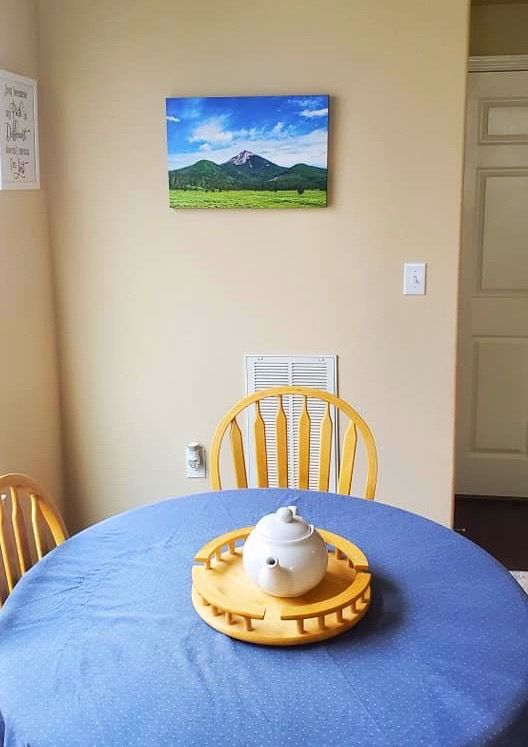 A table setting with turquoise placemat and pottery pieces arranged on a wooden dining table against a beige wall.