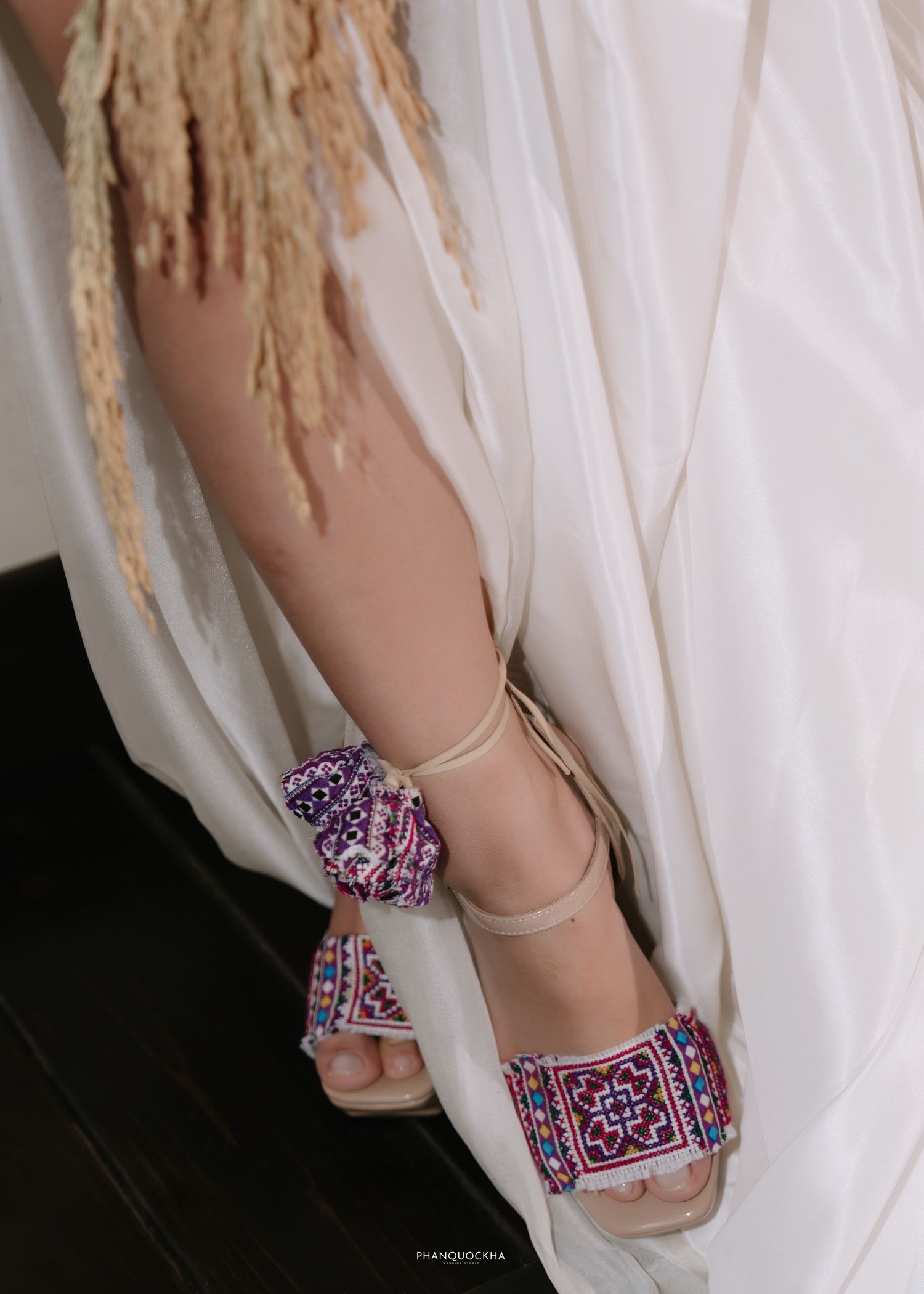 Close-up of bride wearing colorful embroidered heeled sandals with white wedding dress.