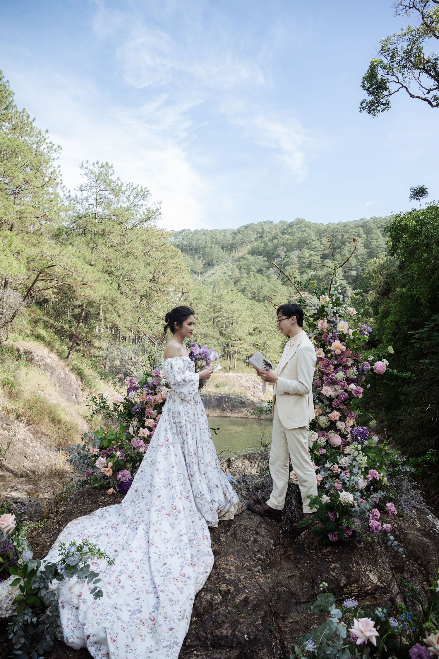 Bride and groom exchange vows on cliff with floral arch and mountain view.