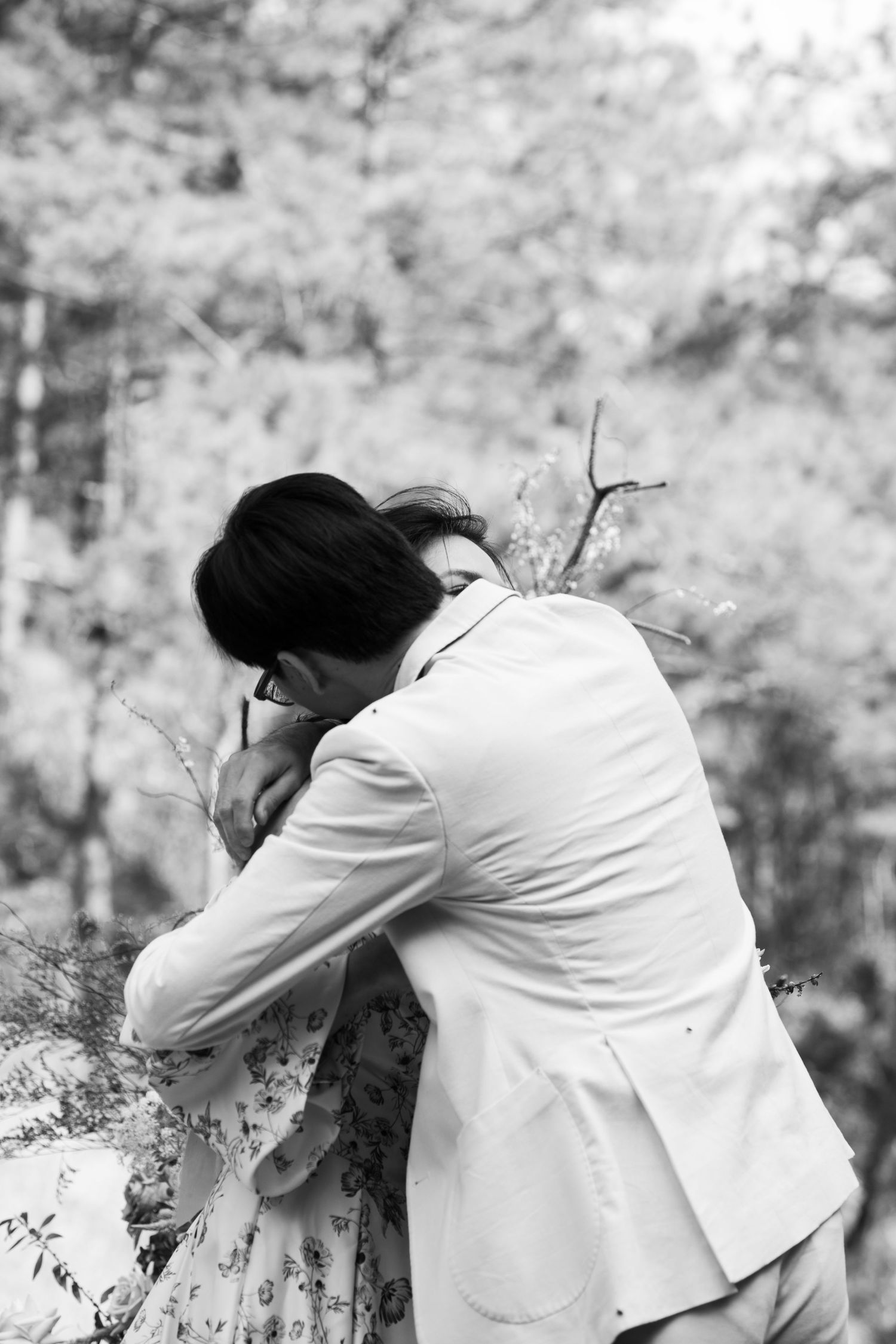 Emotional couple shares tender embrace during outdoor wedding in forest setting.