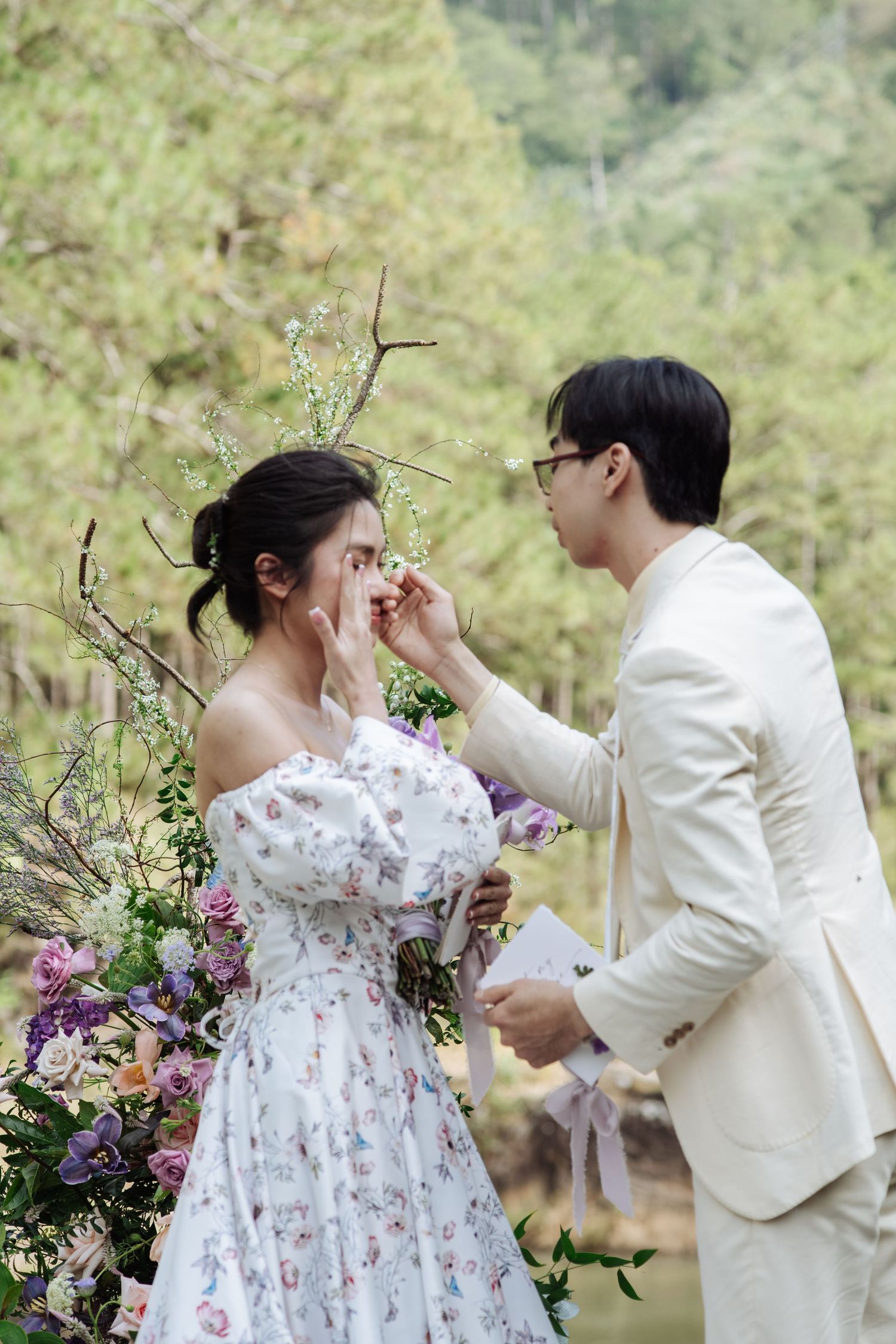Groom gently wipes bride's tears during heartfelt outdoor wedding ceremony.