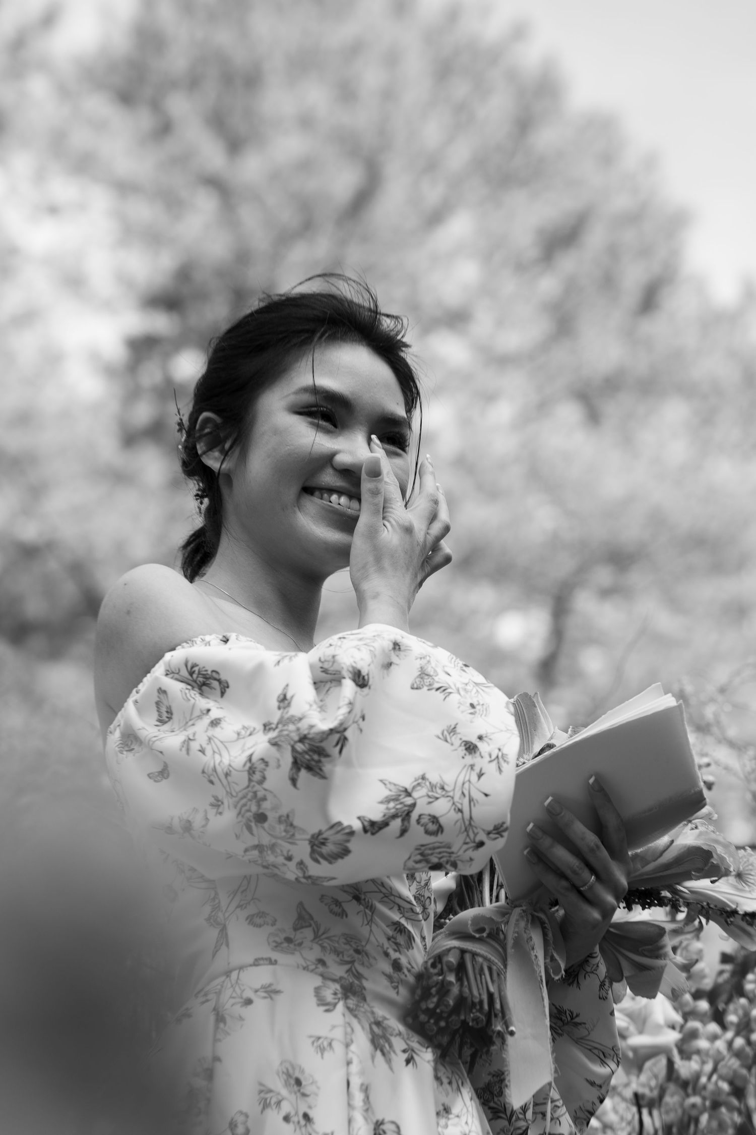 Emotional bride smiles while wiping tears during outdoor wedding ceremony.