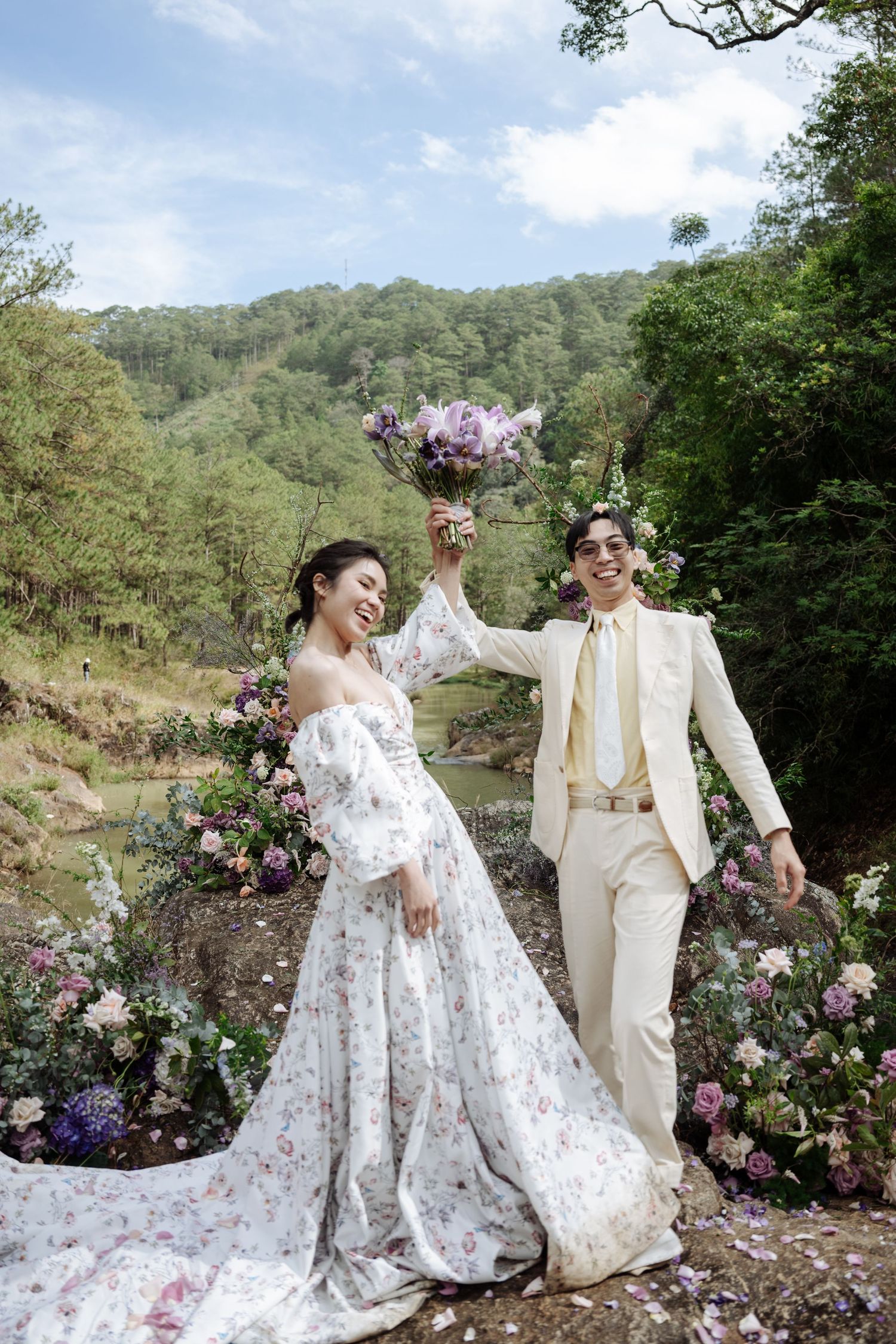 Joyful bride and groom celebrate outdoors with bouquet raised high amid lush floral decor.