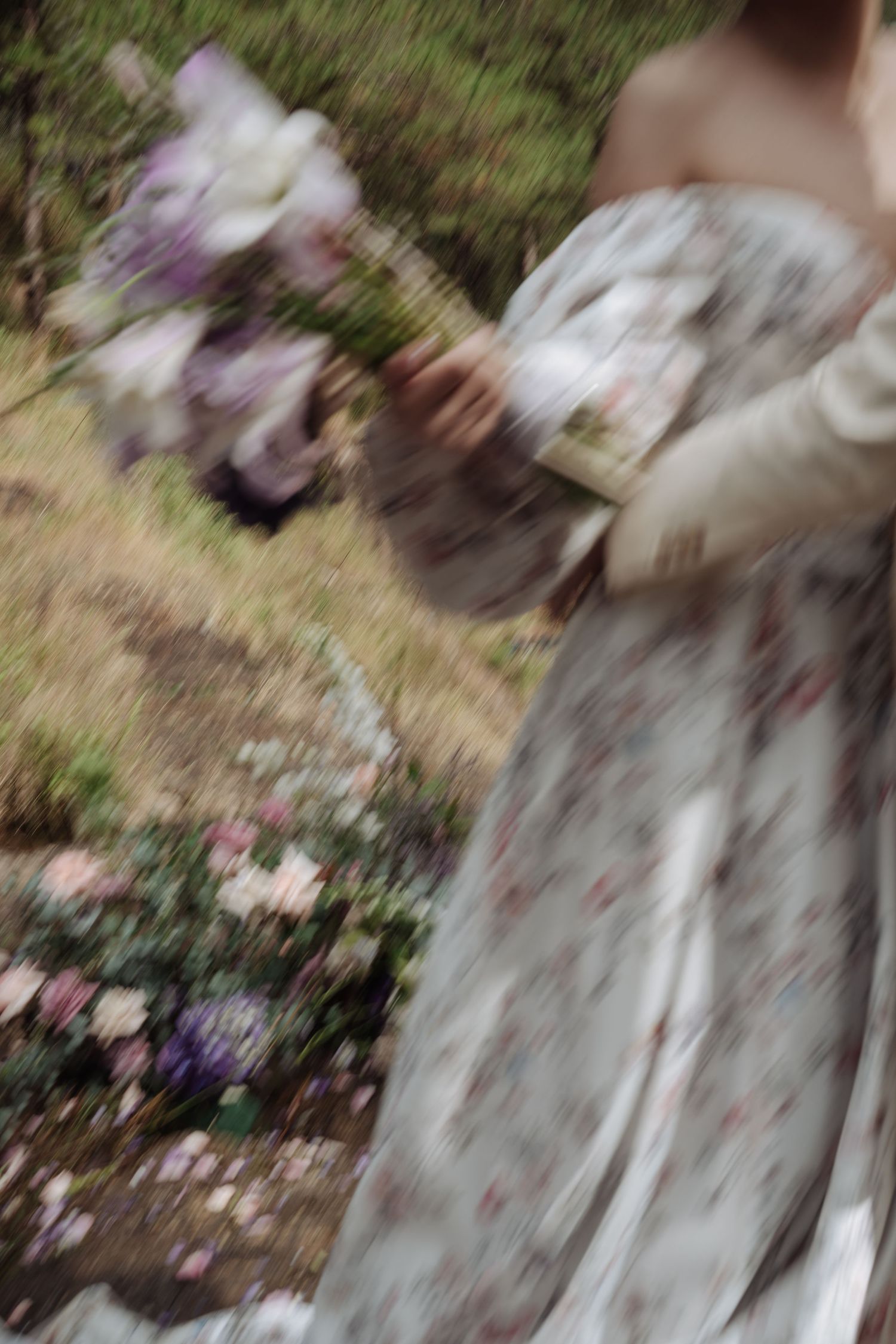 Artistic blurred motion shot of bride in floral gown holding bouquet in garden setting.