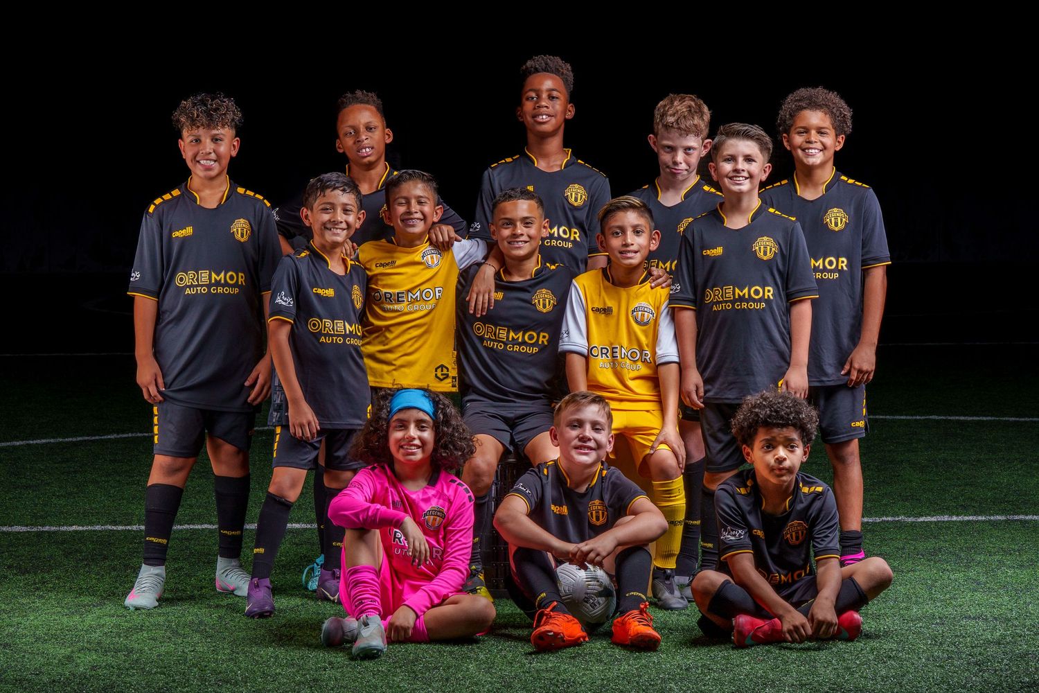 Soccer team members in blue and yellow uniforms gather for group photo on turf field.