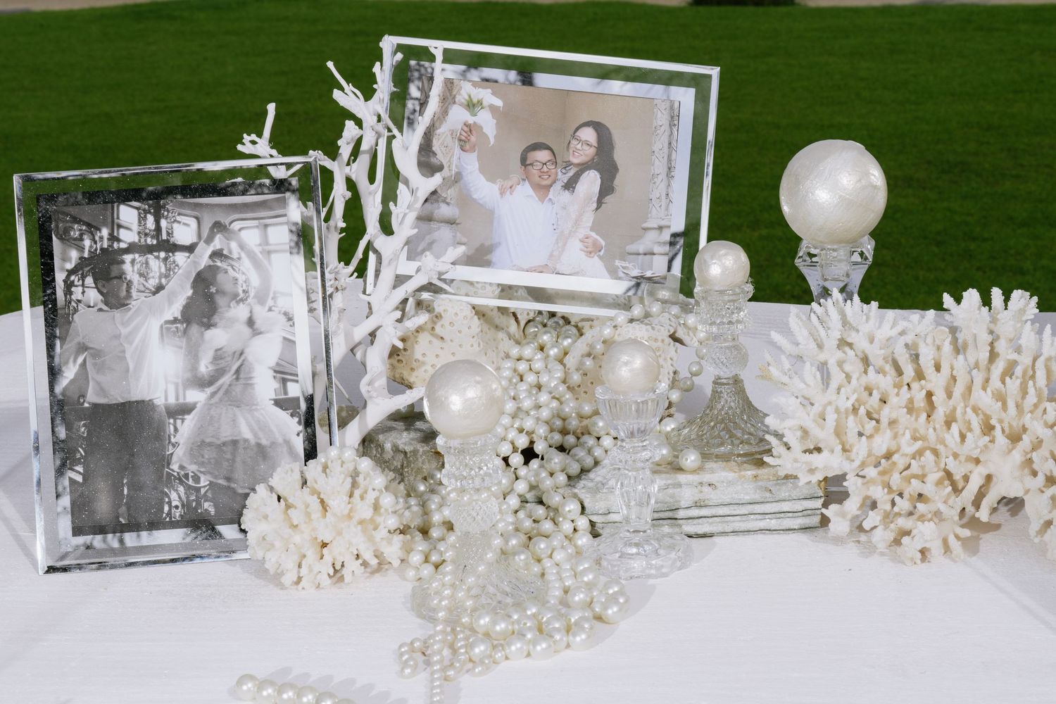 White wedding table display with pearl decorations, coral pieces, crystal frames, and couple photographs.