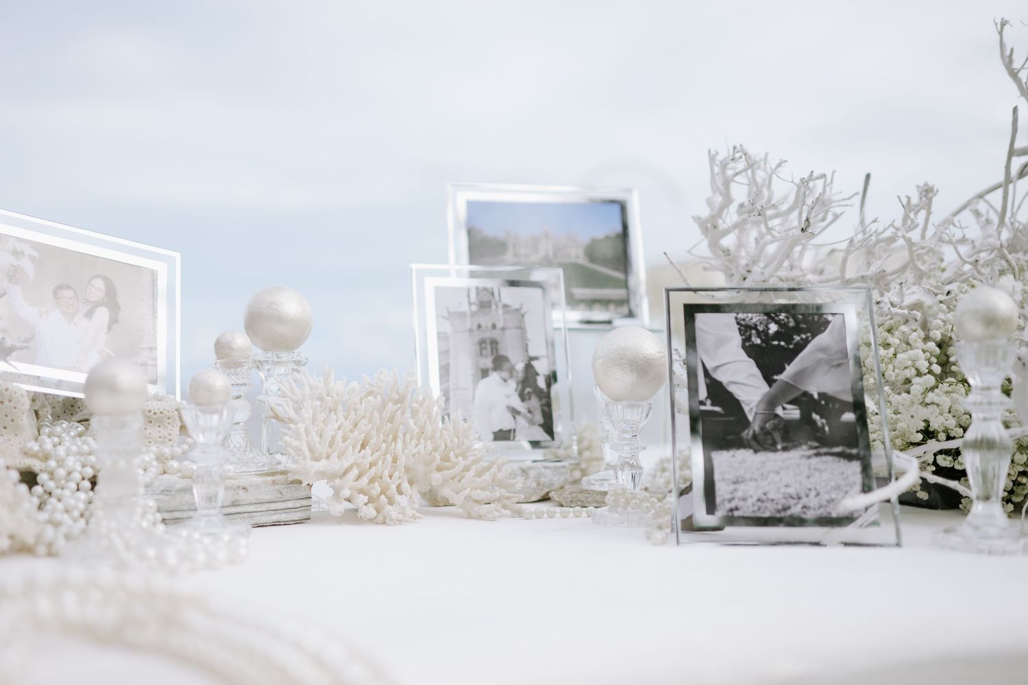 White wedding table display featuring framed black and white photos, coral accents, and pearl decorations.