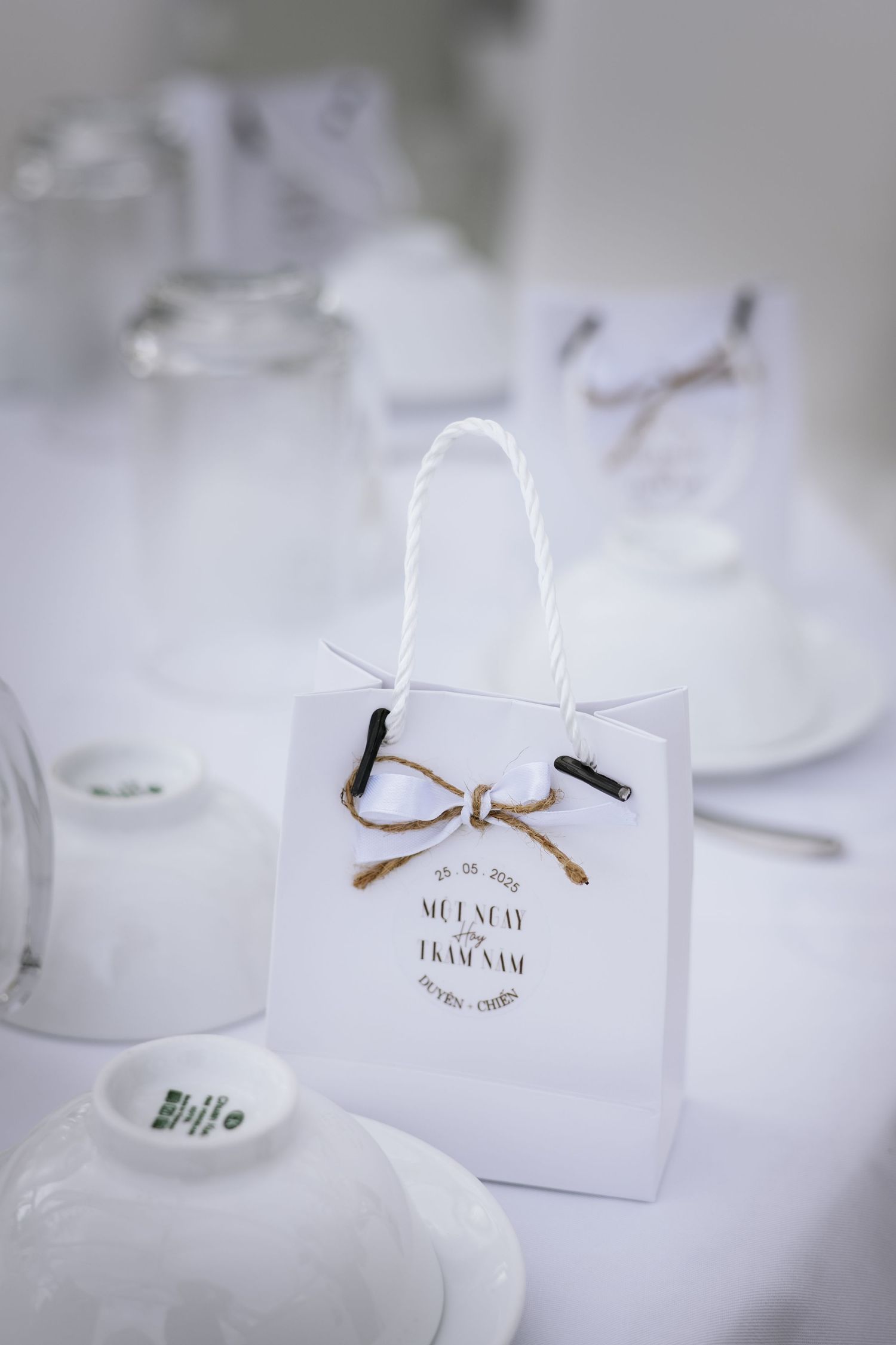 White wedding favor gift bag with couple's names printed, tied with twine bow on reception table.