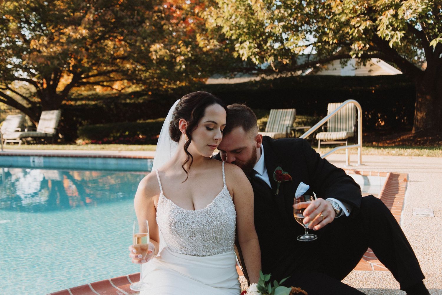Newlyweds share an intimate moment while sitting at the edge of a swimming pool during autumn.