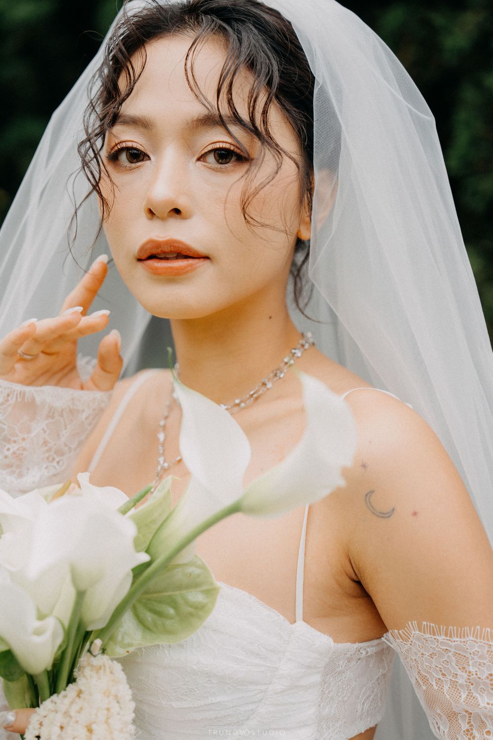 Close-up portrait of a bride in a lace wedding dress holding white calla lilies with a veil.
