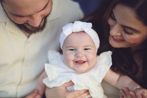 A close-up portrait of a happy baby in white dress with parents.