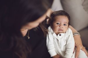A small child wearing a white sweater sits while someone gently styles their hair.