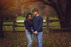 A couple shares romantic moments in a fall park setting with colorful autumn leaves scattered on the ground.